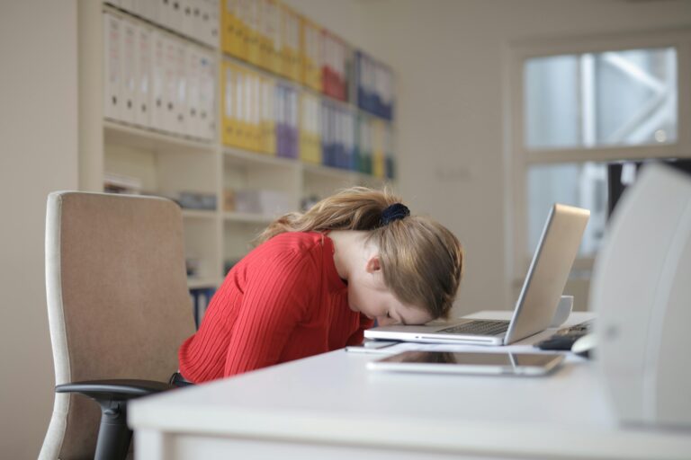 A woman sitting at a desk with her head on a laptop